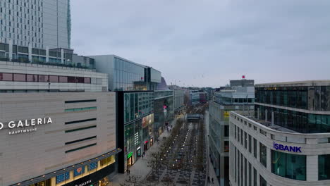 Wide-pedestrian-zone-surrounded-by-multistorey-buildings-with-various-shops.-Forwards-fly-above-Zeil-shopping-street-at-twilight.-Frankfurt-am-Main,-Germany