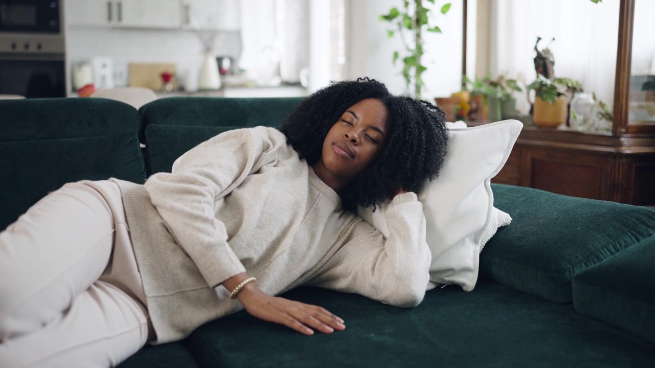 Fredfyldt ung afroamerikansk kvinde sover på sofaen derhjemme