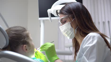 Friendly-female-dentist-examines-teeth-of-a-cute-little-girl-using-her-instruments.-Shot-in-4k