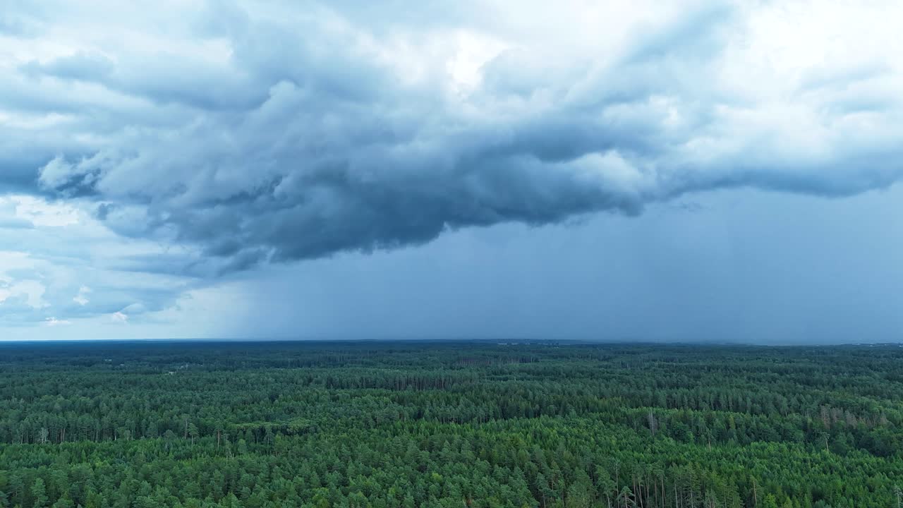 Powerful dark storm clouds forming above woodland landscape, aerial time lapse view