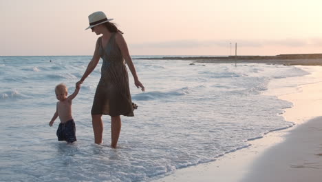 Mother-holding-baby-hand-at-beach.-Mom-and-son-enjoying-sunset-at-coastline.