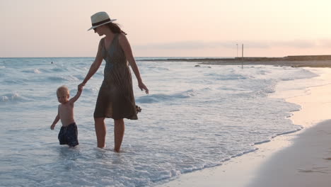 mother holding baby hand at beach. mom and son enjoying sunset at coastline.