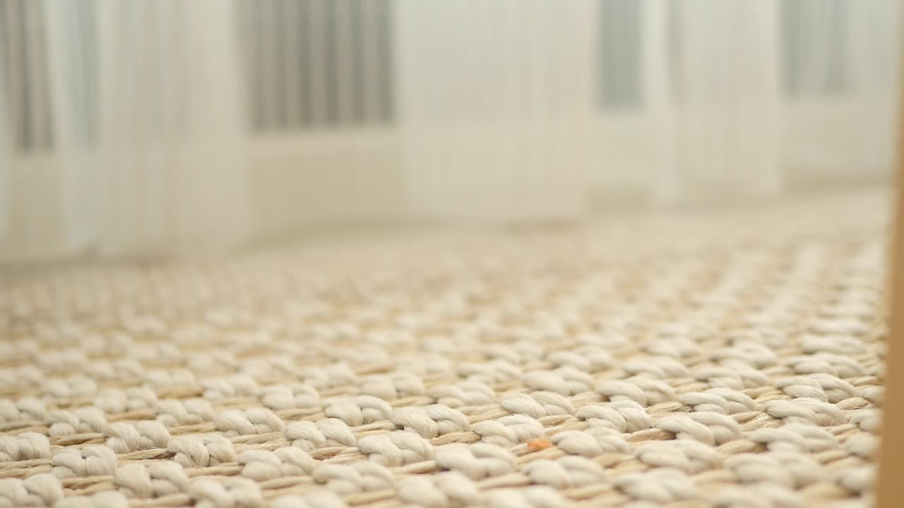 Close-up of a woven rug with sheer curtains in the background