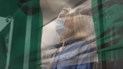 Animation-of-flag-of-nigeria-waving-over-caucasian-woman-wearing-face-mask-in-city-street