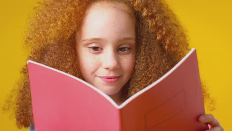 fotografía de estudio de una niña estudiando el libro de ejercicios escolar contra un fondo amarillo