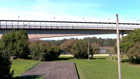 car bridge over the ulla river built hindering in the middle of a garden with trees and shrubs near the water, a sunny afternoon, drone shooting traveling forward