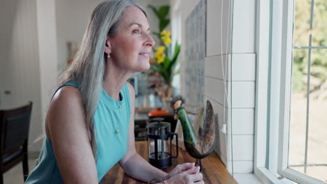 mujer mayor relajándose junto a la ventana en la cocina