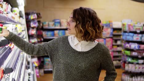 food, health concept - woman in a supermarket standing in front of the freezer shelves and choose buying a bottle of yogurt