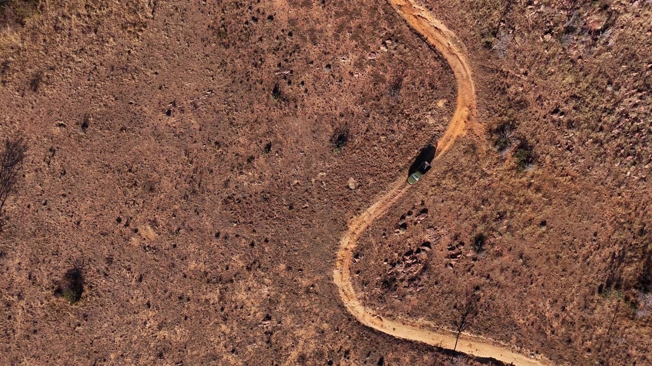 Pemandangan drone dari atas kendaraan 4x4 di jalan tanah berliku di semak belukar Afrika.