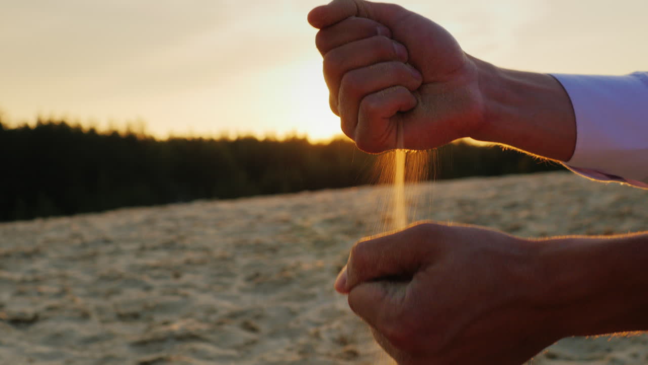 arenas se deslizan a través de las manos del hombre en un traje 1