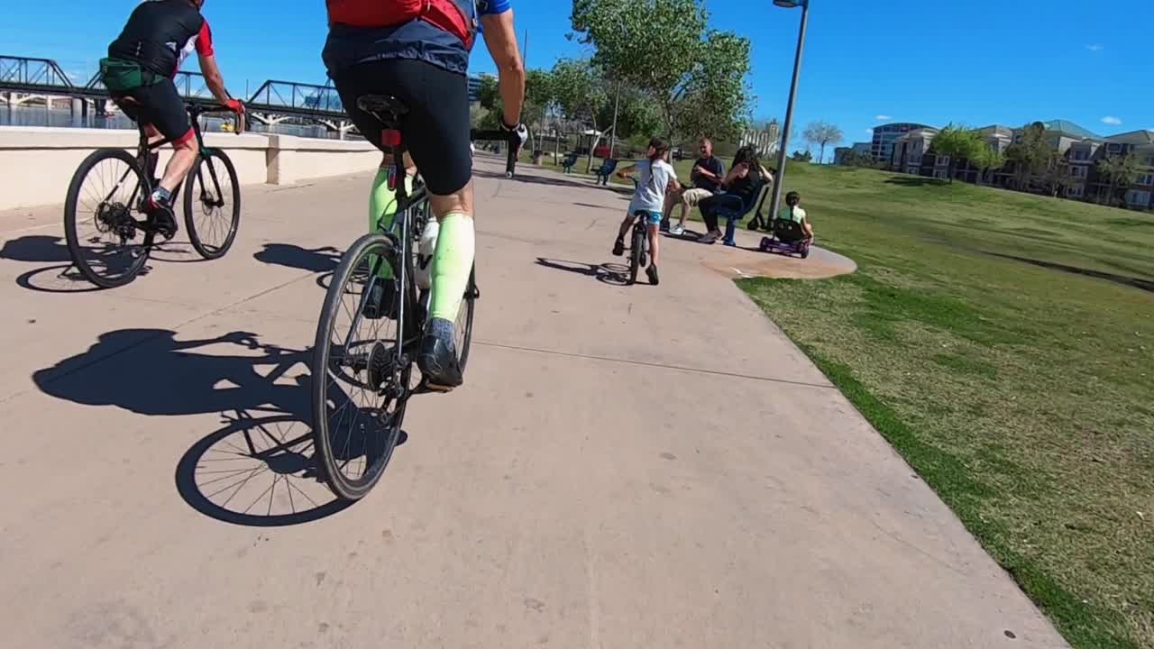 POV skateboarder follows behind three bicycles as they ride down the South Shore Tempe Town Lake Shore walkway, Tempe, Arizona.