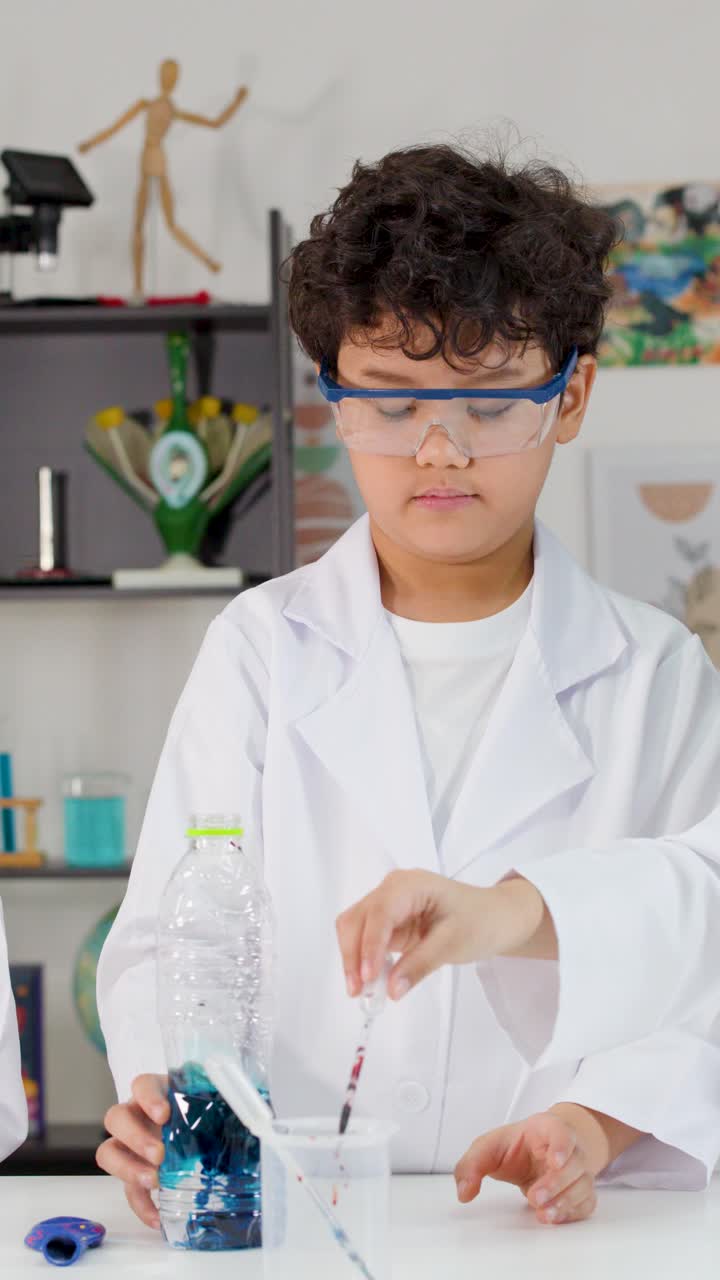 To børn i laboratoriekittel og beskyttelsesbriller bruger pipetter til at blande farvede væsker i flasker.