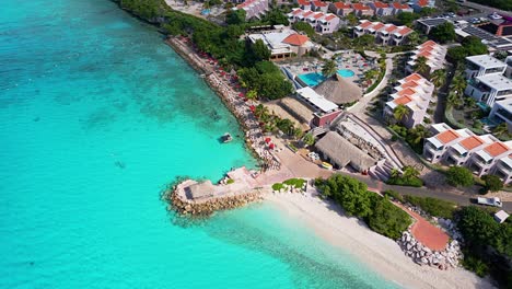 Die-Drohne-Erhebt-Sich-Kippend-über-Dem-Weißen-Sandstrand-Mit-Tischen-Und-Blick-Auf-Den-Karibischen-Ozean