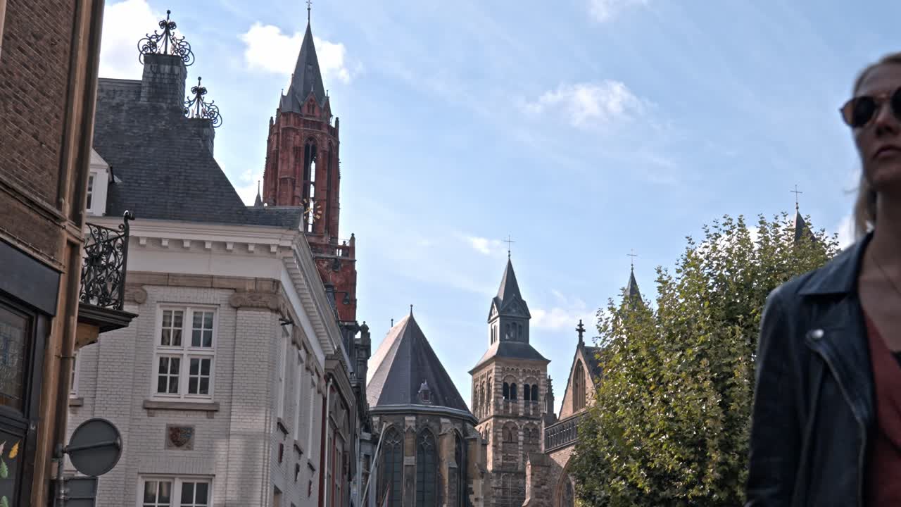 Woman on Vrijthof square in a sunny day, the historic center of Maastricht, Netherlands. The background is dominated by the iconic red tower of the Sint-Janskerk (St. John's Church)