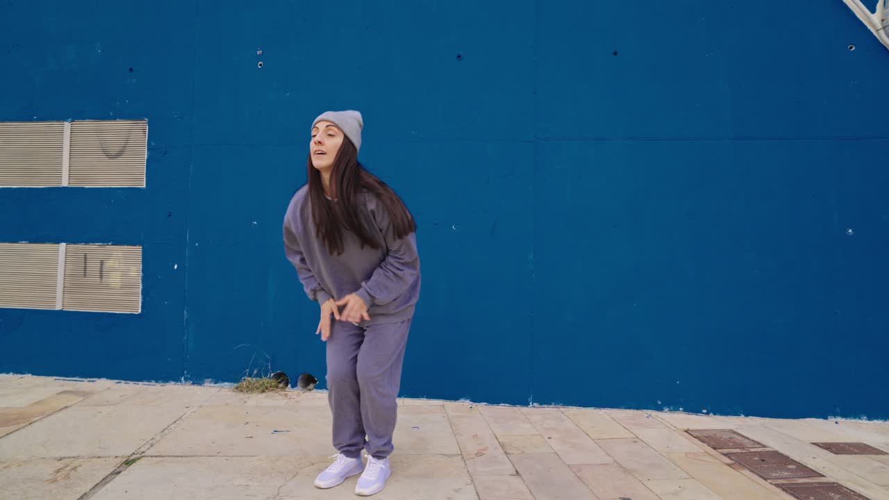 Woman dancing hip hop in front of a blue wall