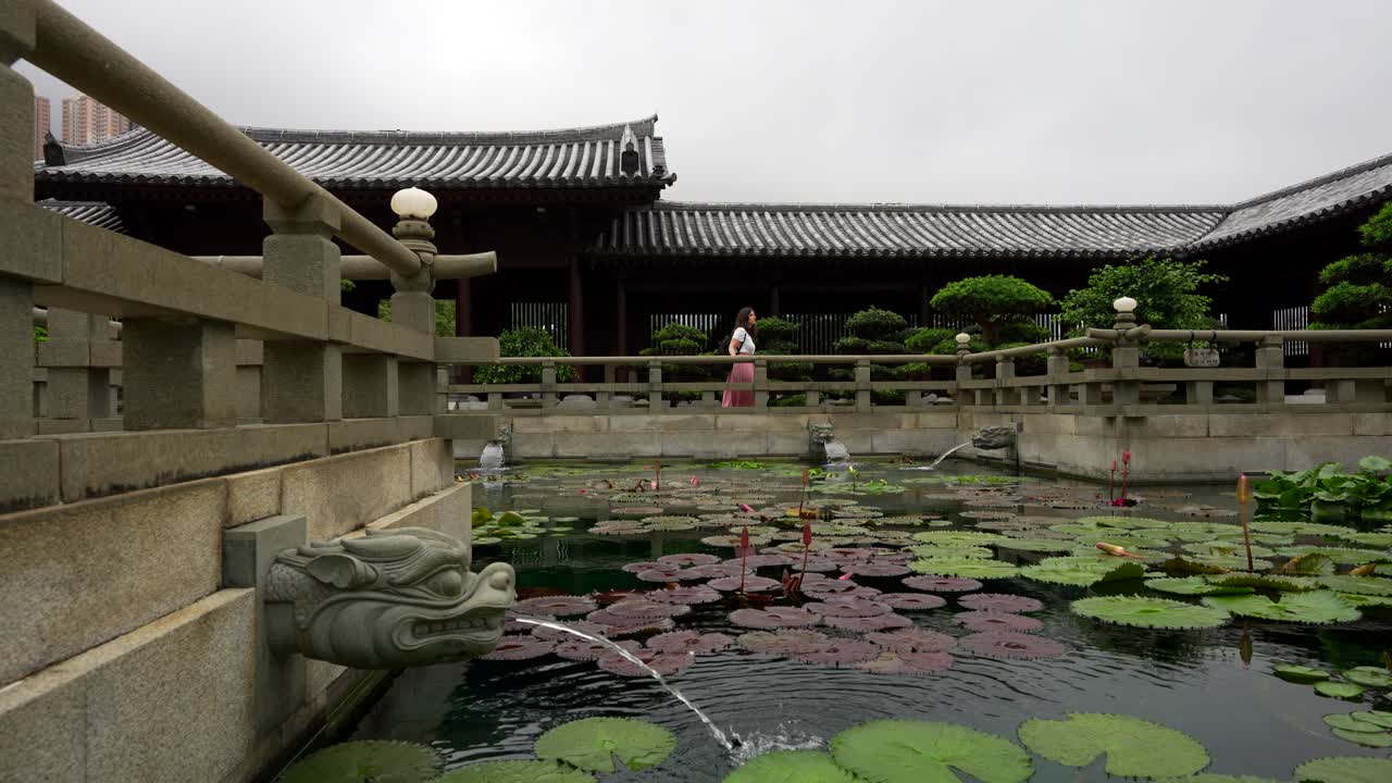 una mujer explora el jardín nan lian cerca de un estanque de lirios de agua con tuberías en forma de dragón, hong kong, china