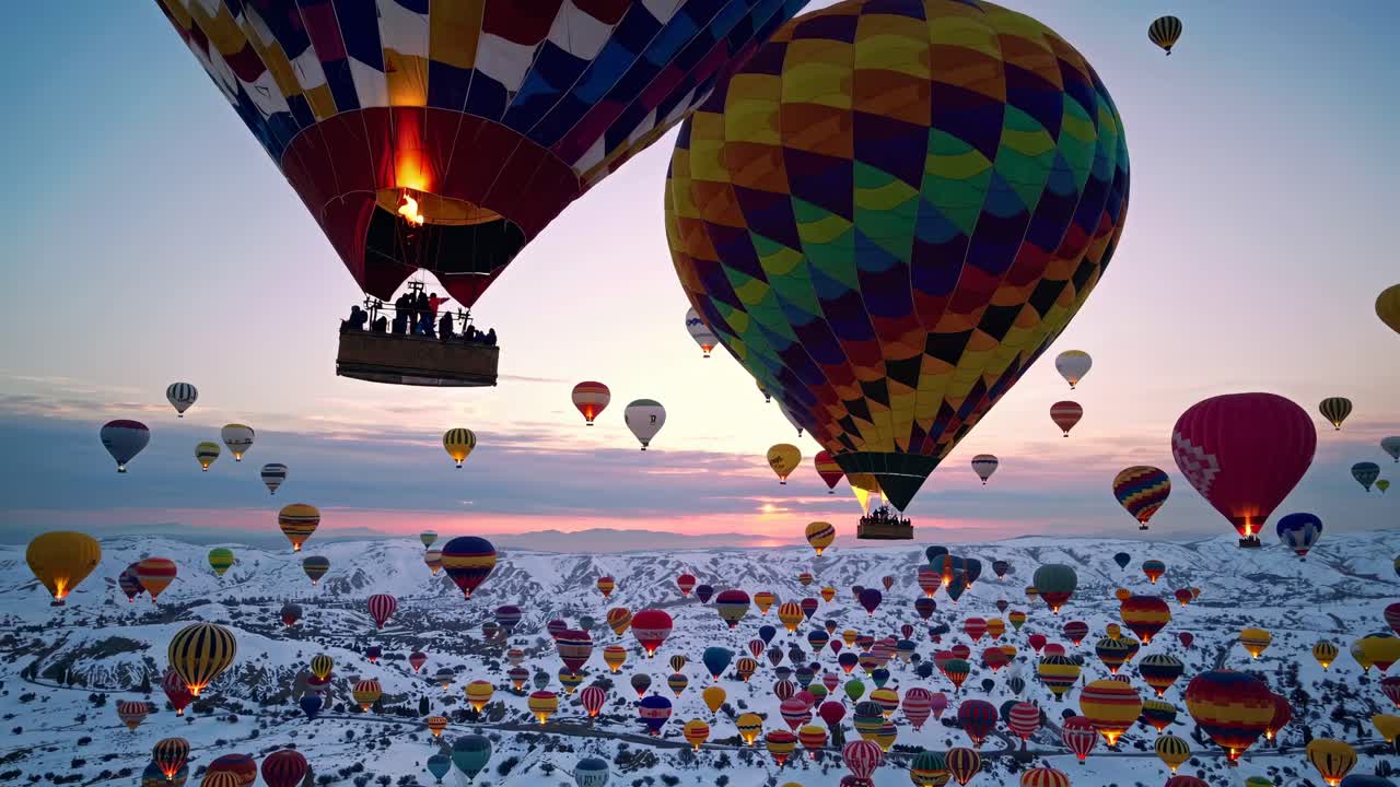 Aerial view of colorful hot air balloons floating over snowy landscapes at sunrise