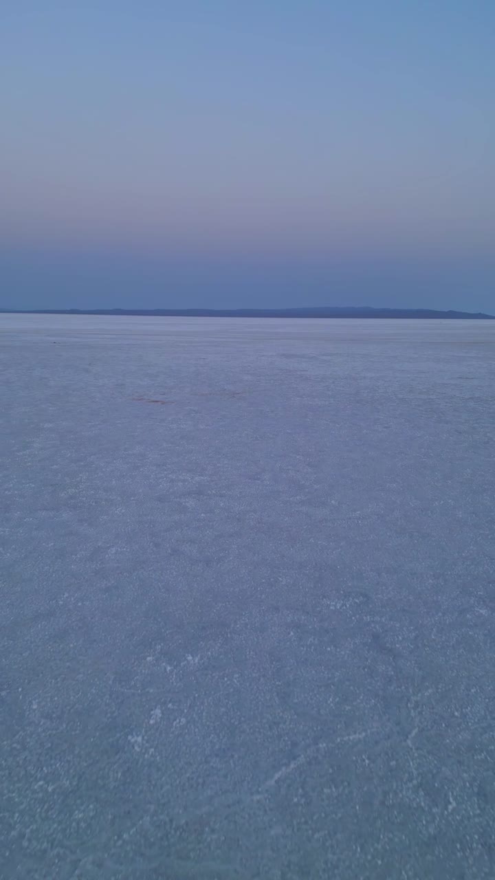 A backward aerial view of the Rann of Kutch India reveals the endless white salt desert glowing softly under the warm hues of the evening sky, creating a serene, magical desert panorama 4K