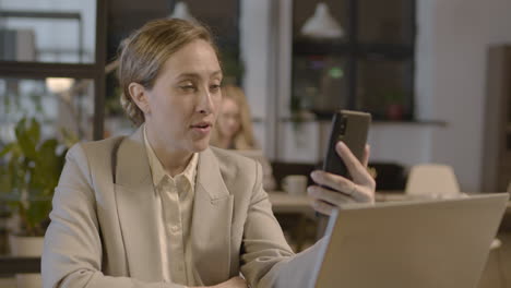 mujer de negocios sonriente que tiene una videollamada con el teléfono móvil mientras trabaja en la oficina