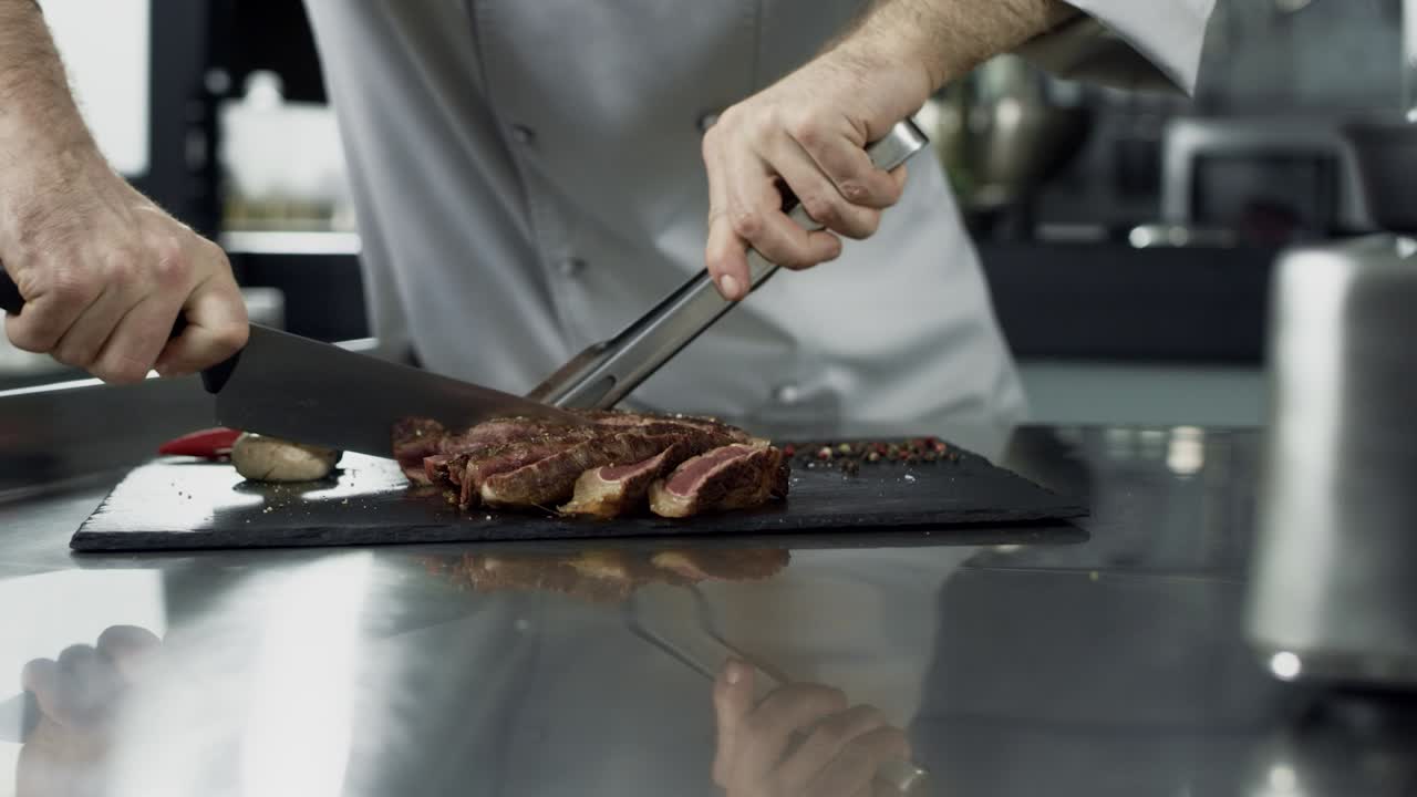 Chef uomo che taglia una bistecca nella cucina del ristorante. Primo piano delle mani dello chef che tagliano la carne.