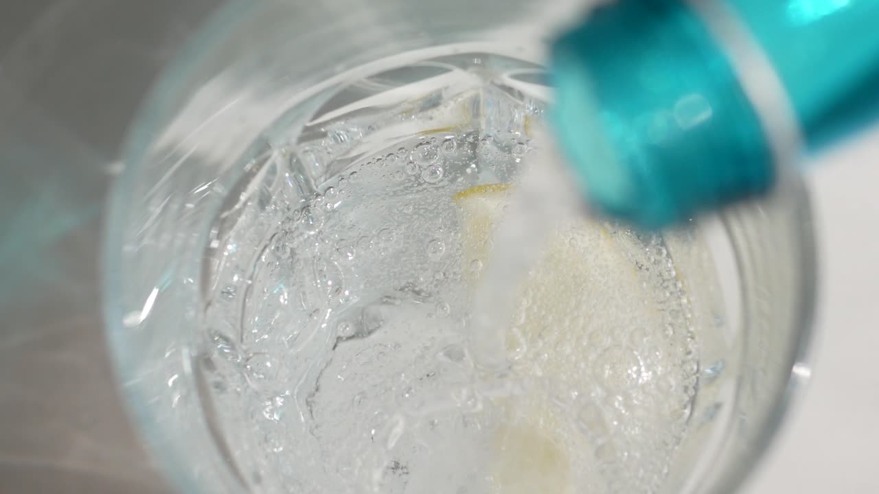 Pouring Soda Water with Lemon and Ice into a Glass