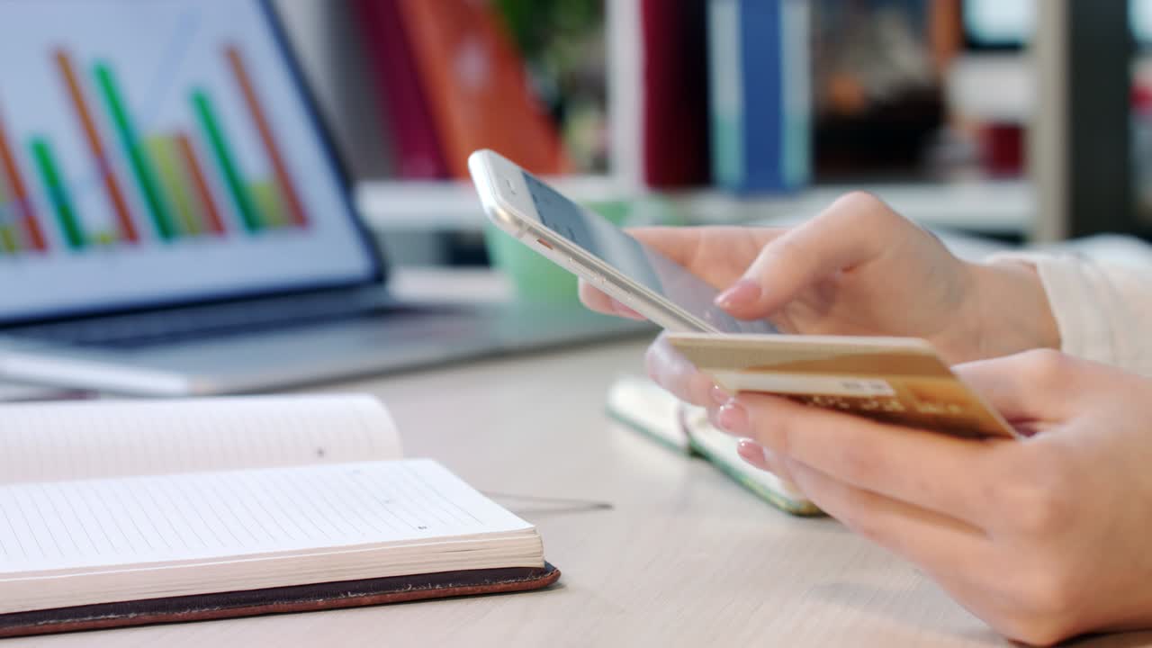 manos femeninas con tarjeta de crédito y teléfono. mujer escribiendo el número de tarjeta de crédito