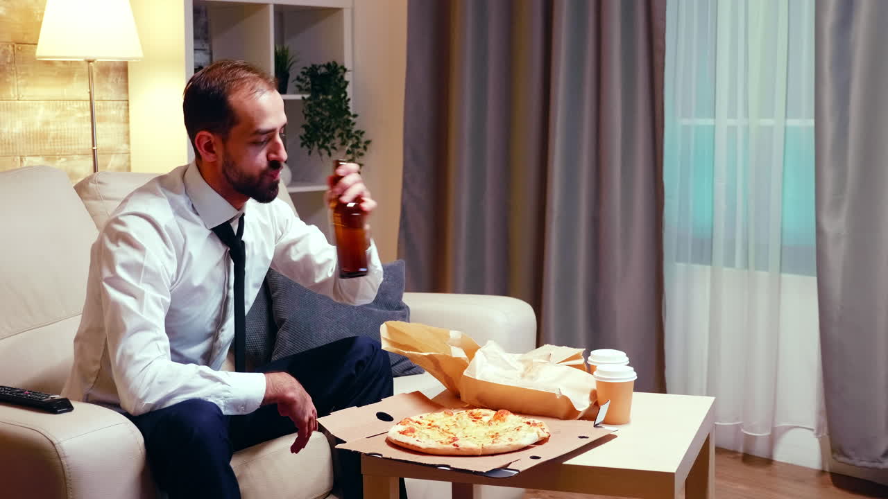 Businessman resting on the couch drinking beer and eating pizza
