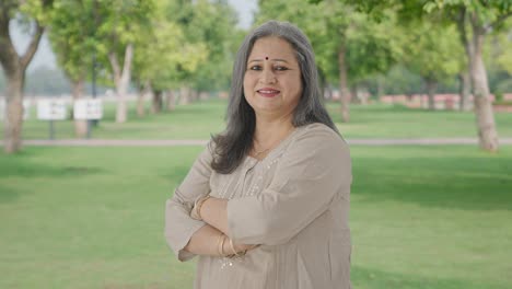 Retrato-De-Una-Anciana-India-Feliz-De-Pie-Con-Las-Manos-Cruzadas-En-El-Parque