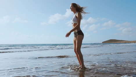 chica con pantalones cortos y camiseta deportiva realiza saltos con sentadillas en la playa cerca del océano en las islas canarias. estilo de vida saludable y fitness en vacaciones. cuerpo hermoso y saludable