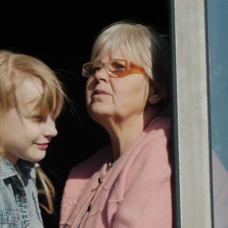 senior woman next to the child sits on the window sill and looks out the window