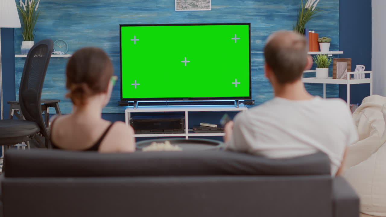 Static tripod shot of couple having a snack while looking at green screen tv watching a movie