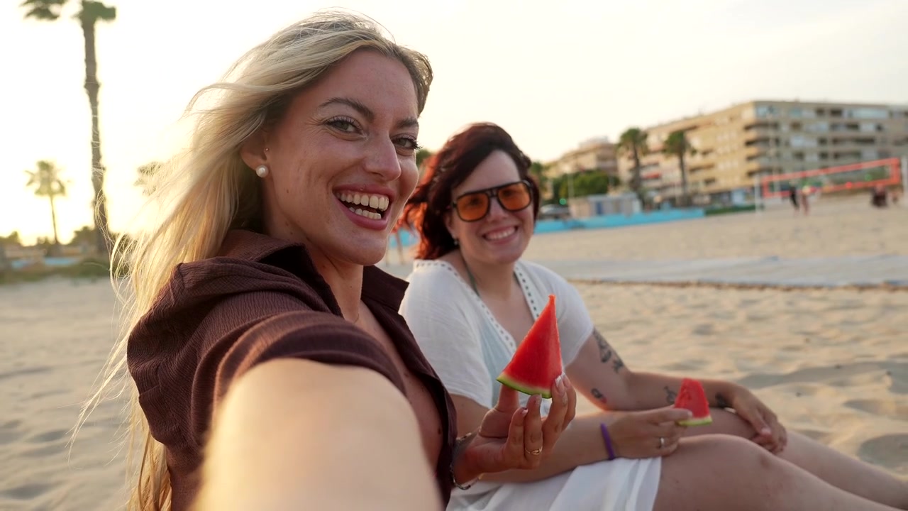 Due donne felici che si scattano un selfie e mangiano anguria in spiaggia