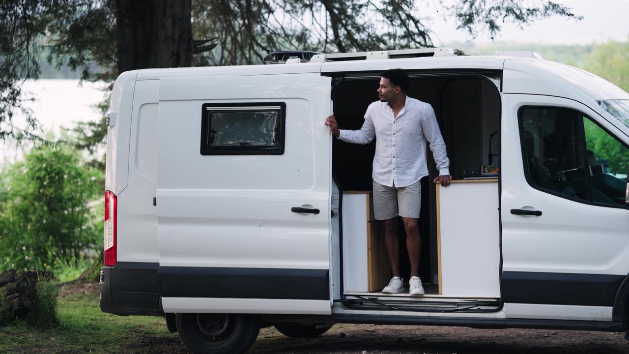 Giovane uomo in piedi sulla porta aperta di un camper nella natura.