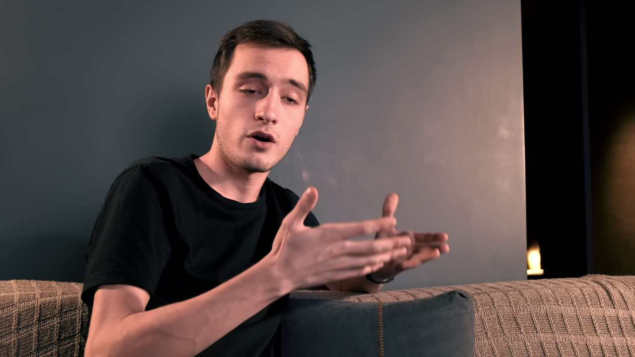 Giovane creator di contenuti che parla e gesticola, usando una fotocamera su un treppiede mentre registra un vlog. Lavora da casa