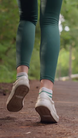corredora femenina corriendo por el camino en el parque. piernas de mujer en zapatos deportivos corriendo por un camino rodeado de árboles. mujer entrenando en la naturaleza en un día de verano
