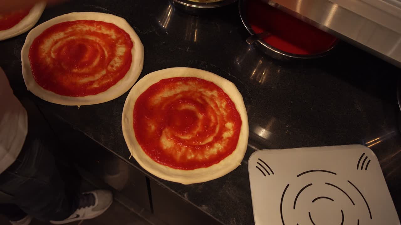 전문 요리사 가 레스토랑 주방 에서 토마토 소스 로 인 피자 반죽 에 바실리 잎 을 첨가 하고 있다