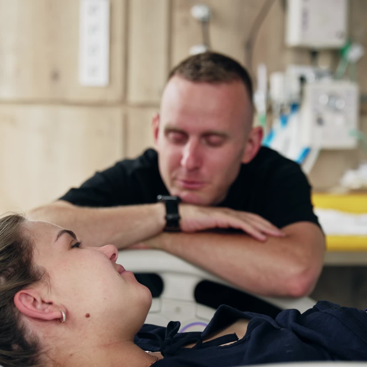 Happy expecting couple in the hospital ward. Man sits next to his wife lying in bed. Expecting spouses talking and laughing