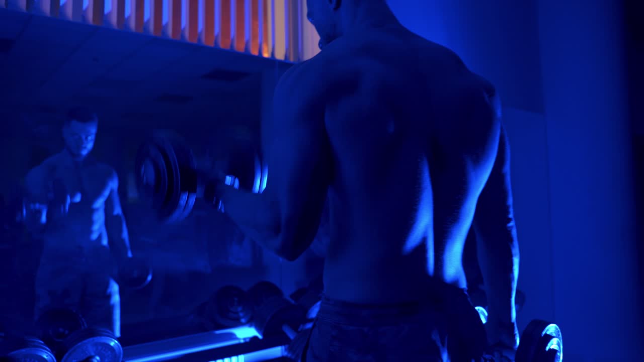 Dambılla egzersiz yapan adam. Spor salonunda dambıl ağırlıklarıyla antrenman yapan vücut geliştirmeci.
