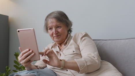 smiling senior woman using tablet while lying on sofa at home 1