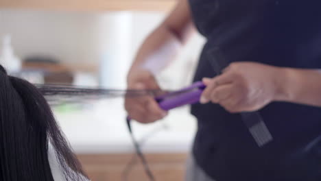 using a hair straightener to on an attractive young black teen's hair before styling it - isolated