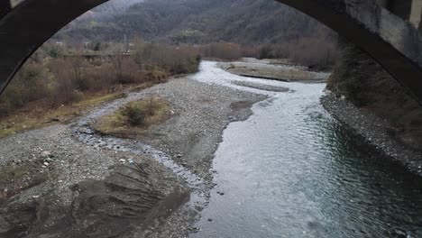 river flowing under an arched bridge in a mountainous valley