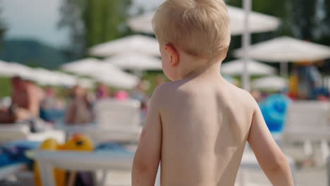 funny boy walks along public beach at resort on hot day