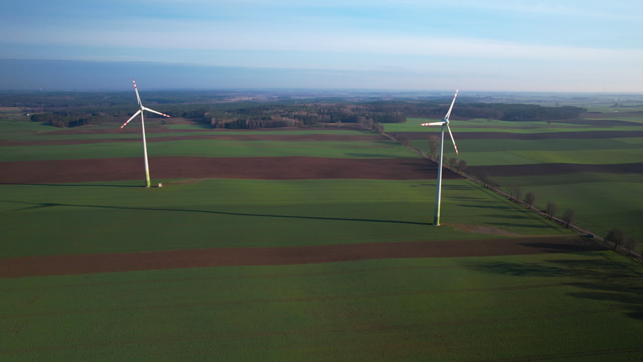 Aerial view of two wind turbines producing green energy on farm field during cloudy day - panorama wide shot