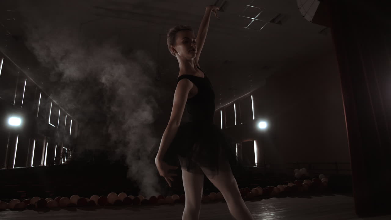Una ballerina aggraziata che esegue elementi di balletto al buio con luce e fumo sullo sfondo, al rallentatore.