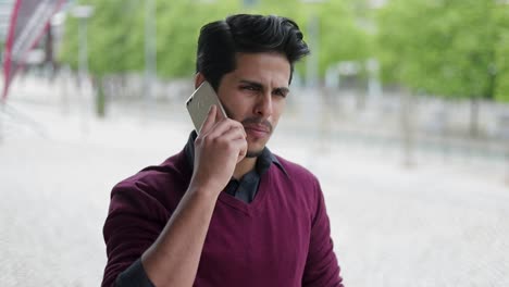 un joven guapo hablando por teléfono afuera, pareciendo serio