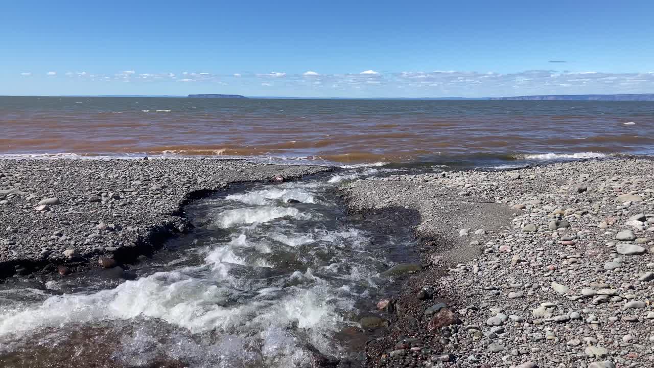Freshwater river mouth stream flowing into saltwater on Atlantic Ocean coastline in Spring