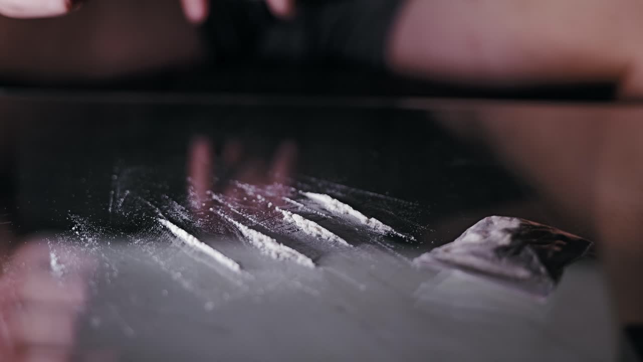 Vista macro, linee di oggetti di scena in polvere bianca su vetro con mano sfocata che si muove dietro