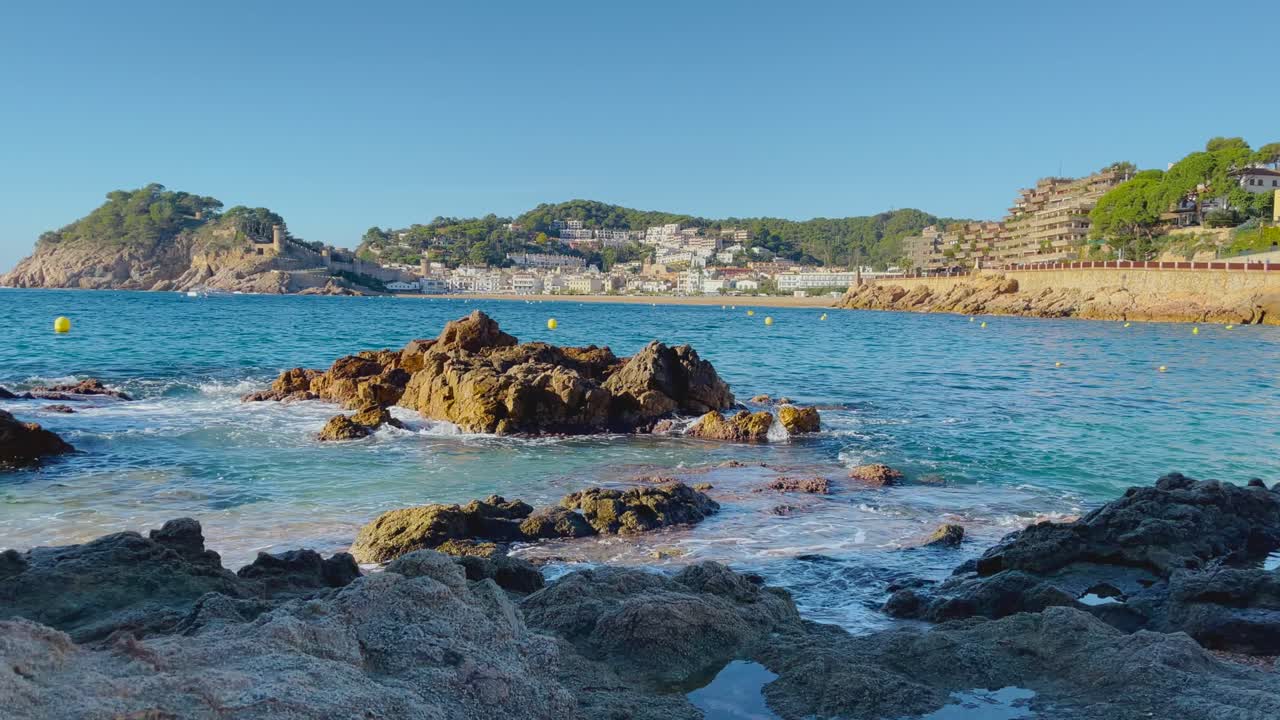 Rotsen op de voorgrond met de baai van Tossa de Mar op de achtergrond, inclusief kasteel en ommuurde vesting.