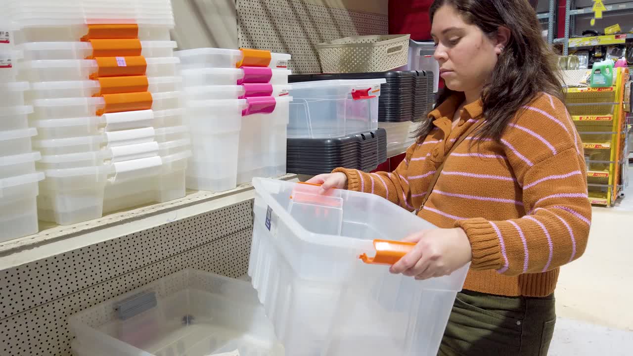 Young woman inspecting a clear plastic storage box in a retail store.