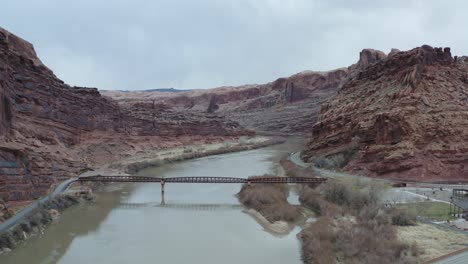 river with bridge in red rock cliff valley in arches national park - aerial